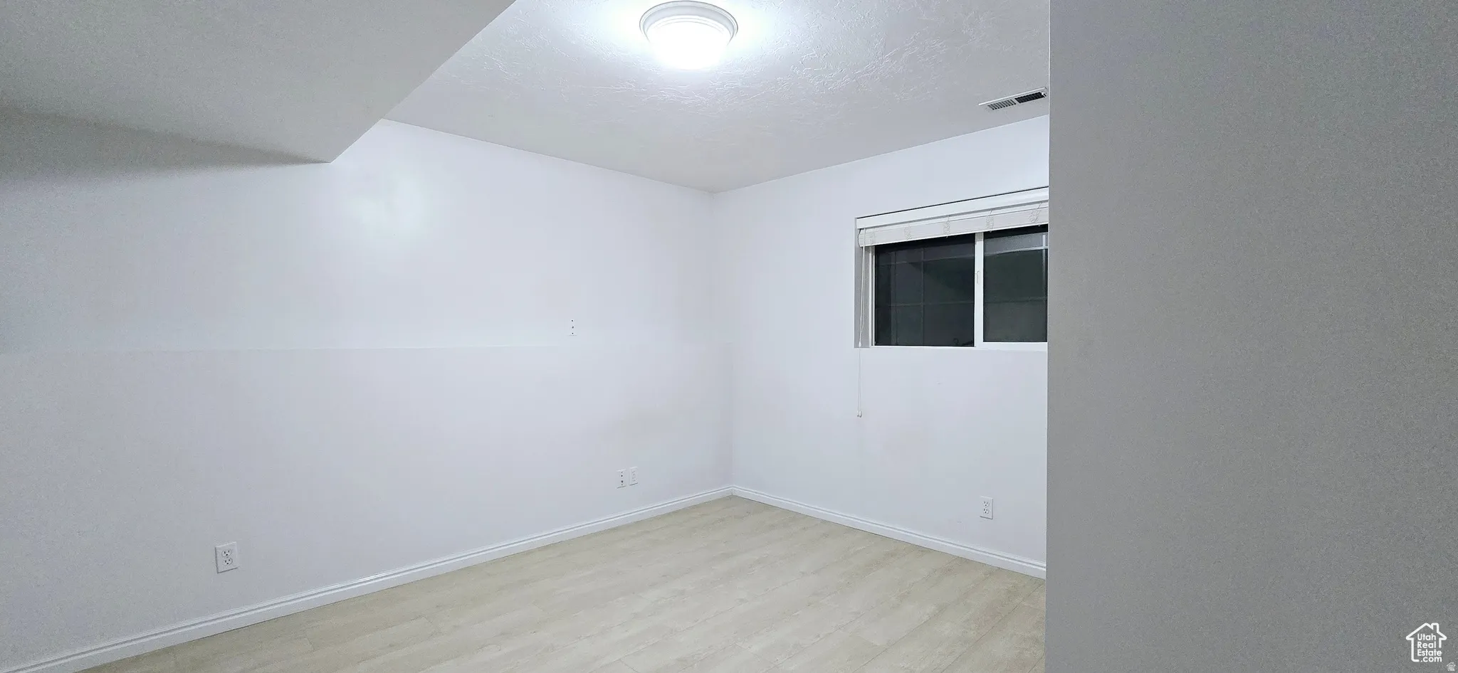 Room featuring light-toned wood-finish flooring, white walls, and a recessed window with blinds