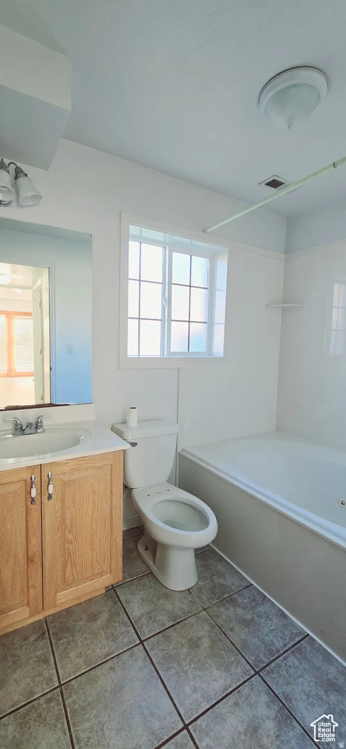 Bathroom featuring a wood-finish vanity with an integrated sink, a white toilet, and a white bathtub with a tiled surround