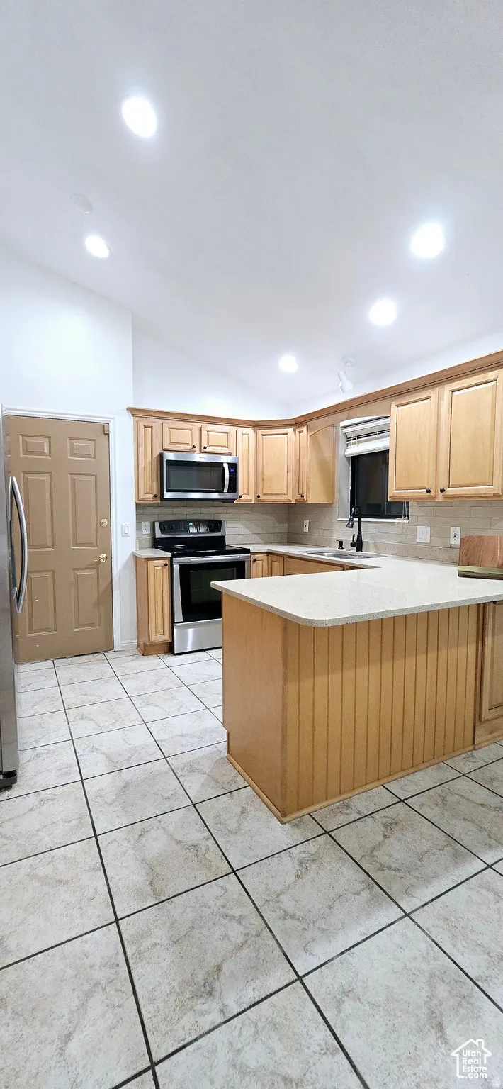Kitchen featuring light wood cabinetry, white countertops, stainless steel appliances, and a tiled floor