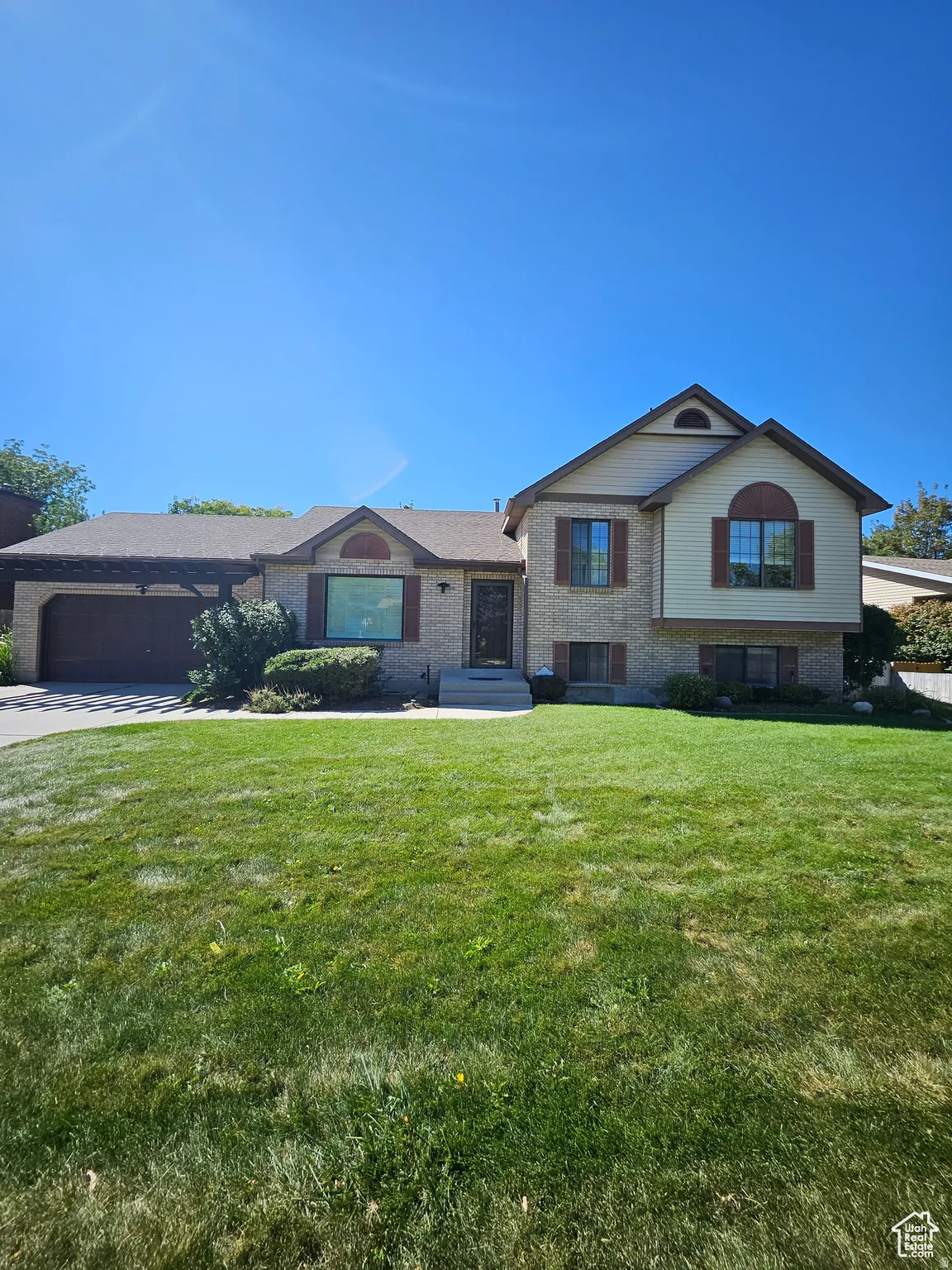 Split-level residence featuring a brick and siding facade, a covered entry, and a two-car garage with an attached pergola