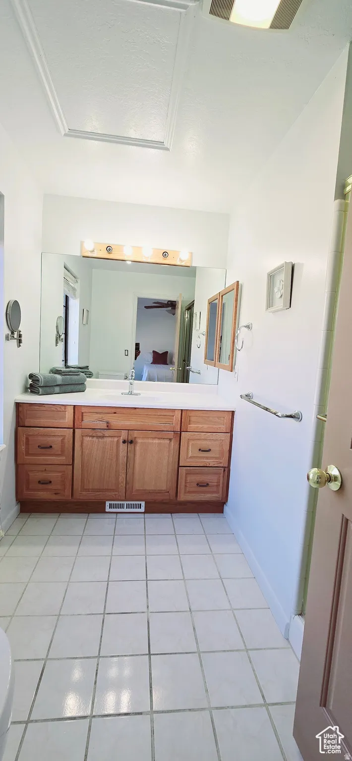 Bathroom featuring a wood-finish vanity with a white countertop and integrated sink, a large wall-mounted mirror, and tile flooring