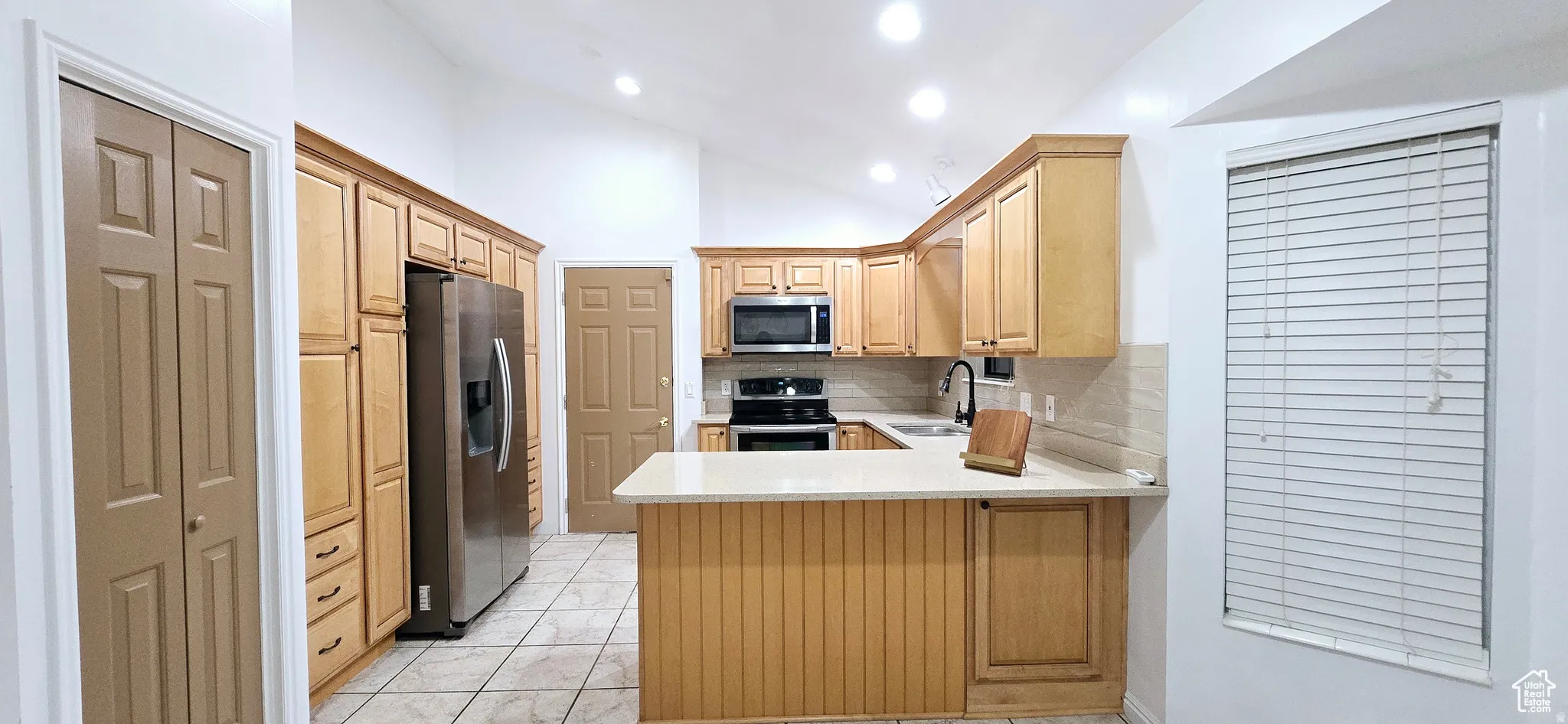Modern kitchen featuring light wood cabinetry, stone-look countertops, and stainless steel appliances
