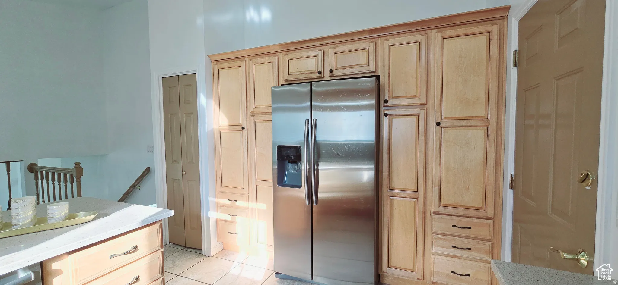 Stainless steel side-by-side refrigerator surrounded by extensive light wood cabinetry