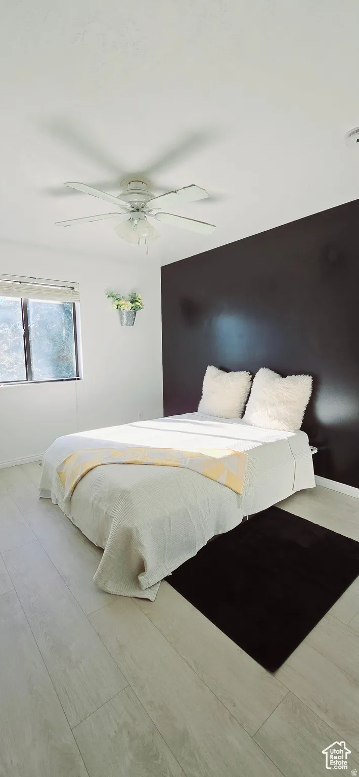 Bright room featuring wood-finish flooring, a ceiling fan, and a prominent dark accent wall