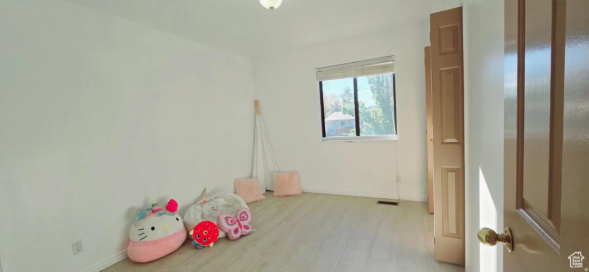 Bright room featuring light wood-finish flooring, a single window with blinds, and a flush mount ceiling light fixture