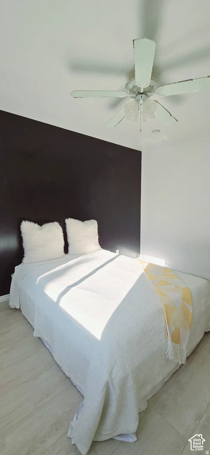 Room featuring a dark accent wall, light wood-finish flooring, and a ceiling fan with integrated lighting
