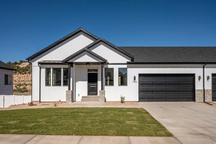 Modern farmhouse style exterior featuring white vertical siding, black trim accents, a black asphalt shingle roof, a two-car garage with a black door, and stone pillar accents