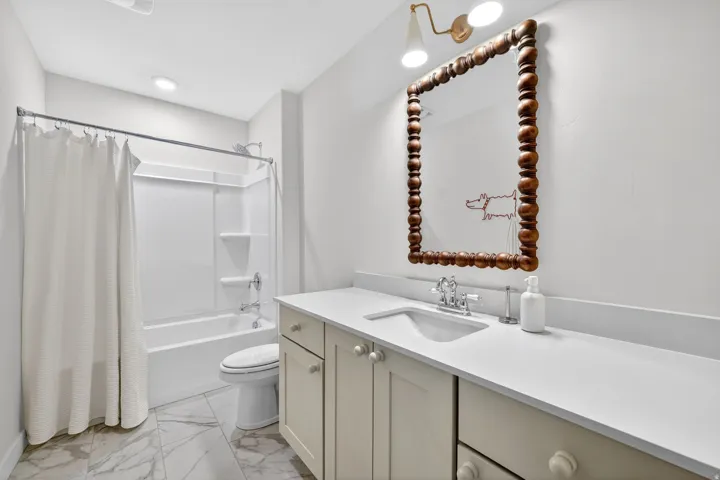 Bathroom featuring a single vanity with a white countertop and light-colored cabinetry, a modern white toilet, and a combination tub/shower with white surround