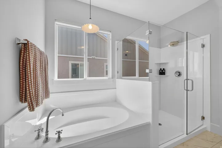 Soaking tub with deck-mounted chrome fixtures, glass-enclosed shower with built-in shelving, white tiled shower surround, and a large window providing ample natural light