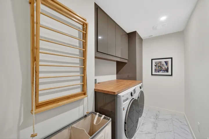 Laundry area featuring stacked appliances, a wood-finish countertop, and high-gloss cabinetry