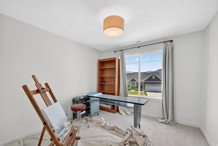 Bright room featuring a large window with white trim, light gray walls, textured carpeting, and a drum pendant light fixture