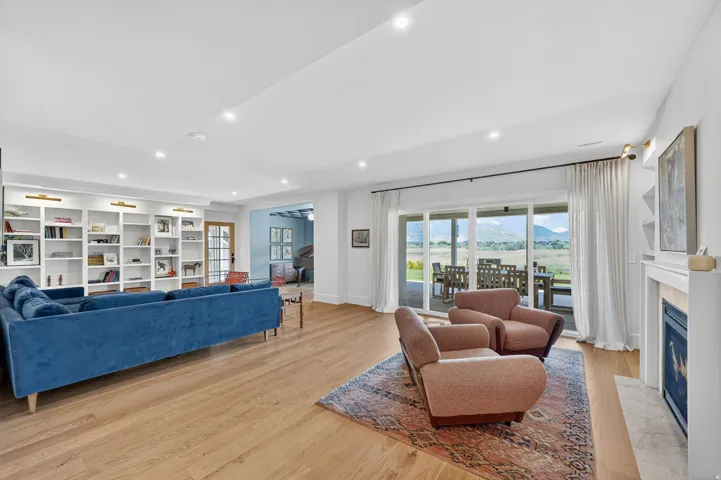 Spacious living area featuring expansive wood-finish flooring, a white mantel fireplace, and recessed lighting