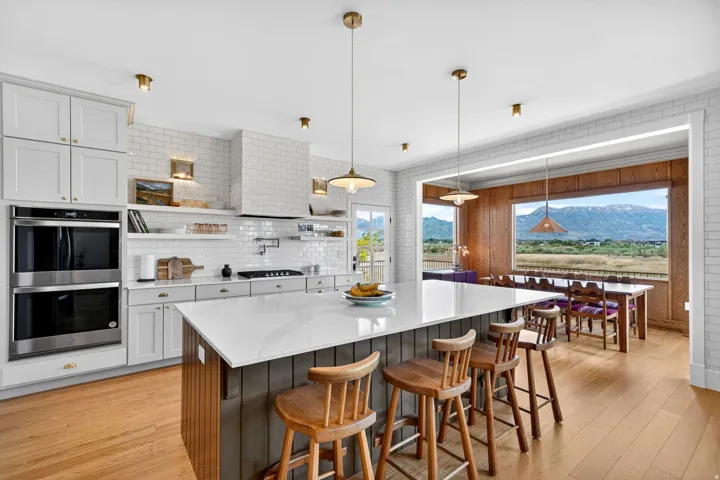 Gourmet kitchen with a large central island featuring a light-toned countertop, white subway tile backsplash, stainless steel double wall ovens, and light wood-finish flooring