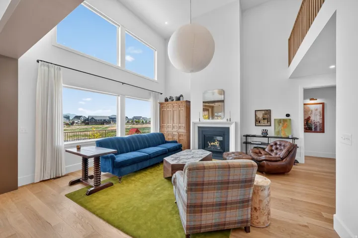 Spacious living area featuring high ceilings, light wood-finish flooring, and a white fireplace with a dark mantel