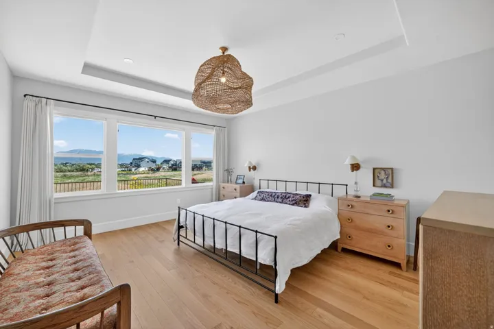 Expansive window wall with mountain and water scenery, featuring light wood-finish flooring, a tray ceiling, and a woven pendant light fixture