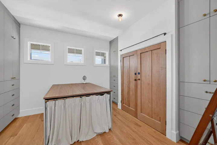 Room featuring custom gray cabinetry with brass hardware, wood-finish flooring, and a central island with a wood countertop