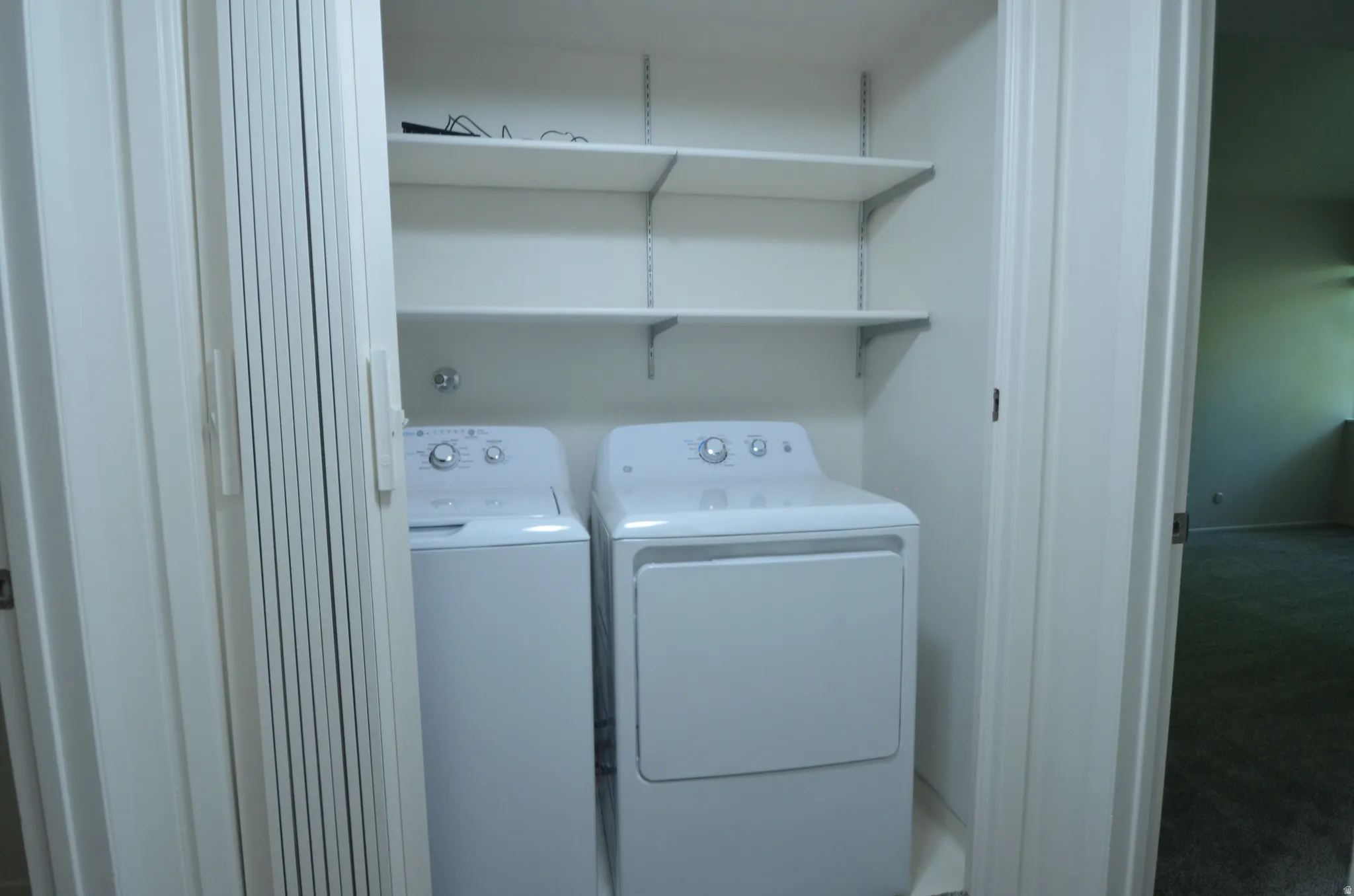 Laundry closet with bi-fold doors, white shelving, and appliance hookups