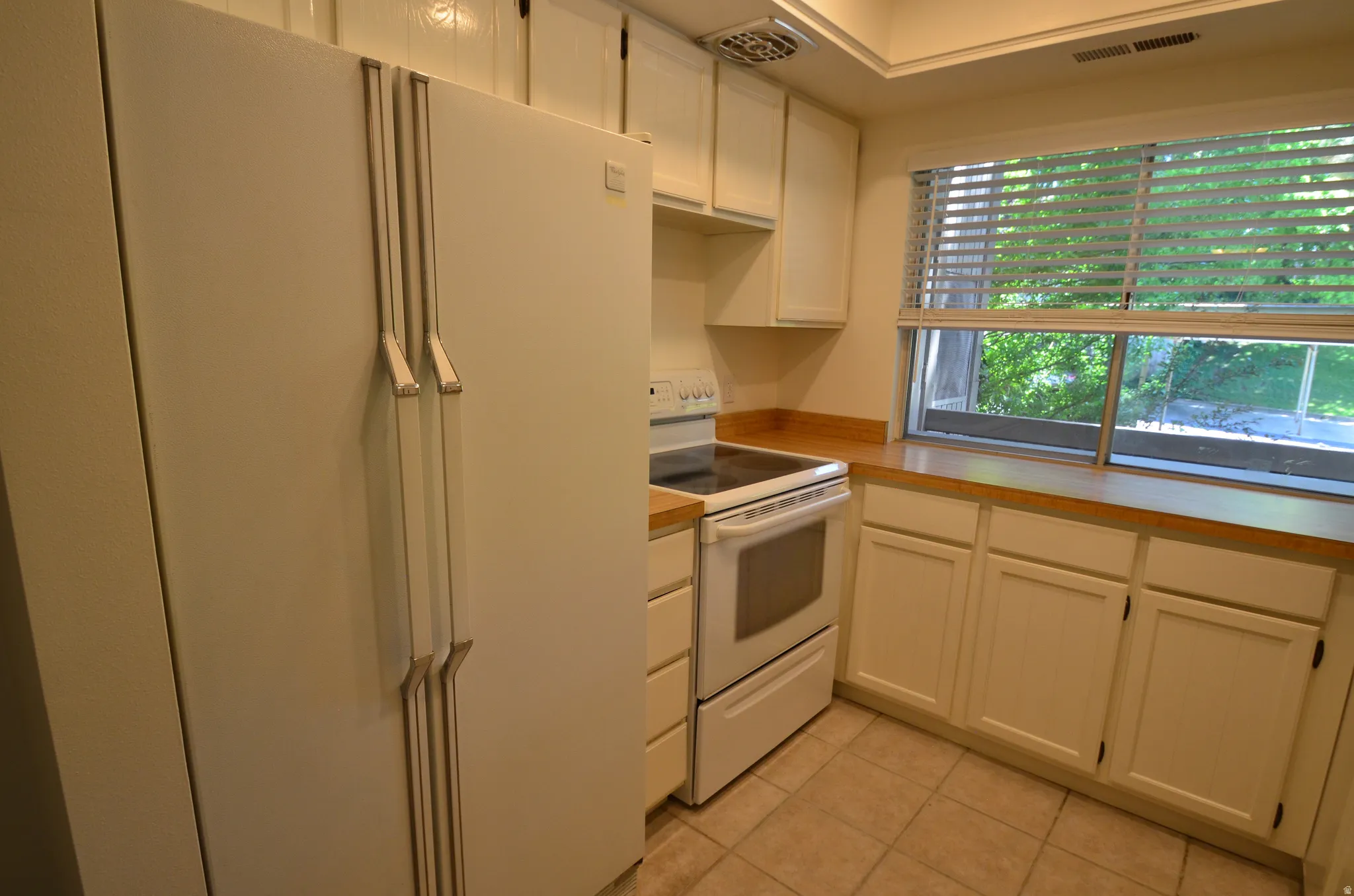Kitchen featuring white cabinetry, wood-finish countertops, white electric range, and a dual-door refrigerator