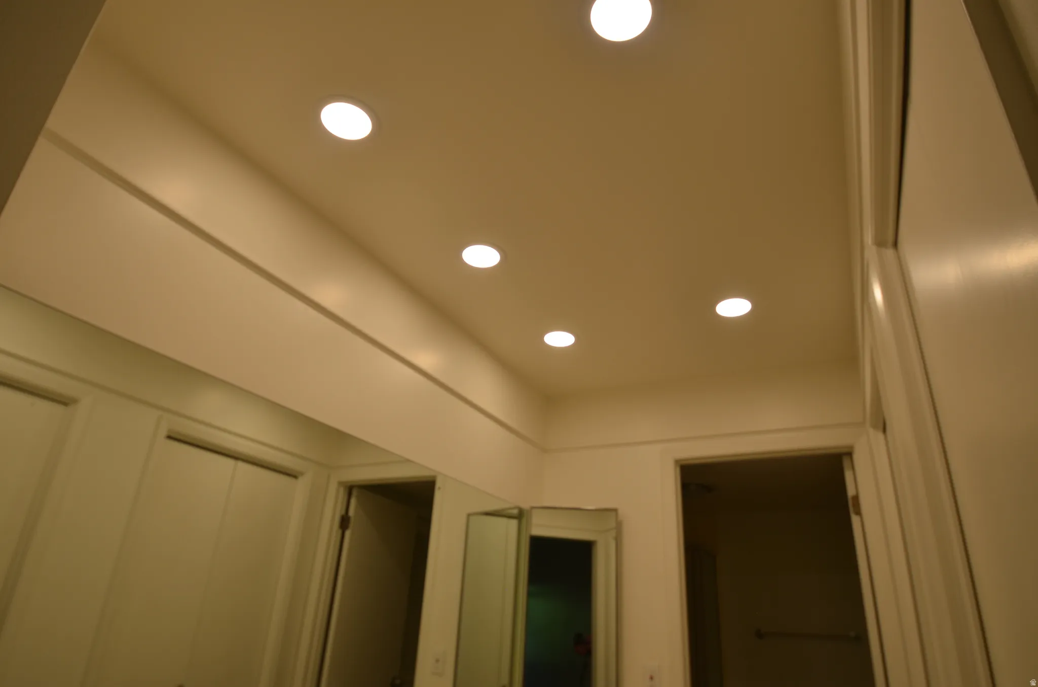 Main bedroom recessed ceiling lighting illuminates the space, featuring a full-width wall mirror and white painted walls