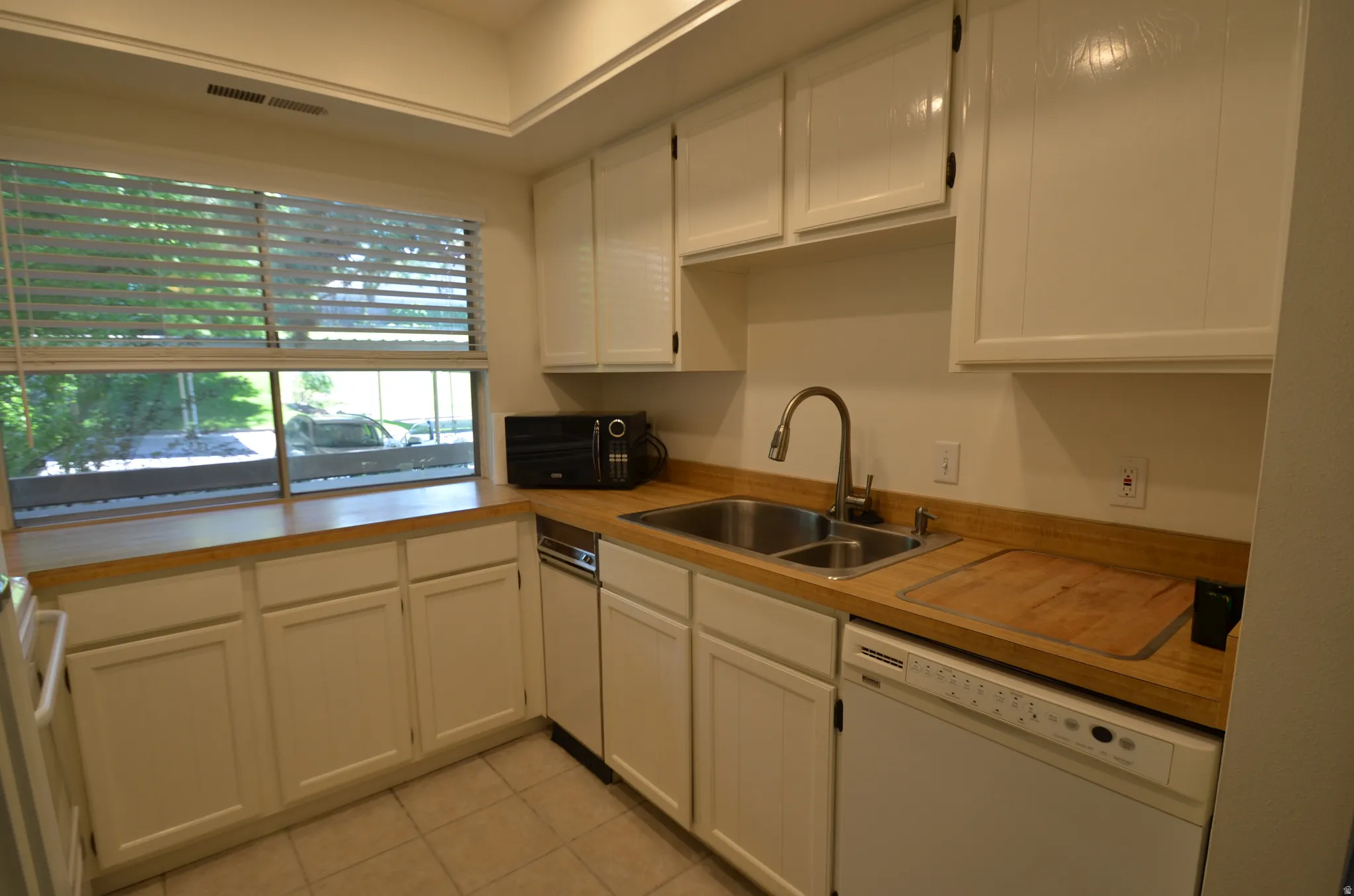 Kitchen featuring white cabinetry, wood-finish countertops, stainless steel double basin sink, and integrated dishwasher and trash compactor