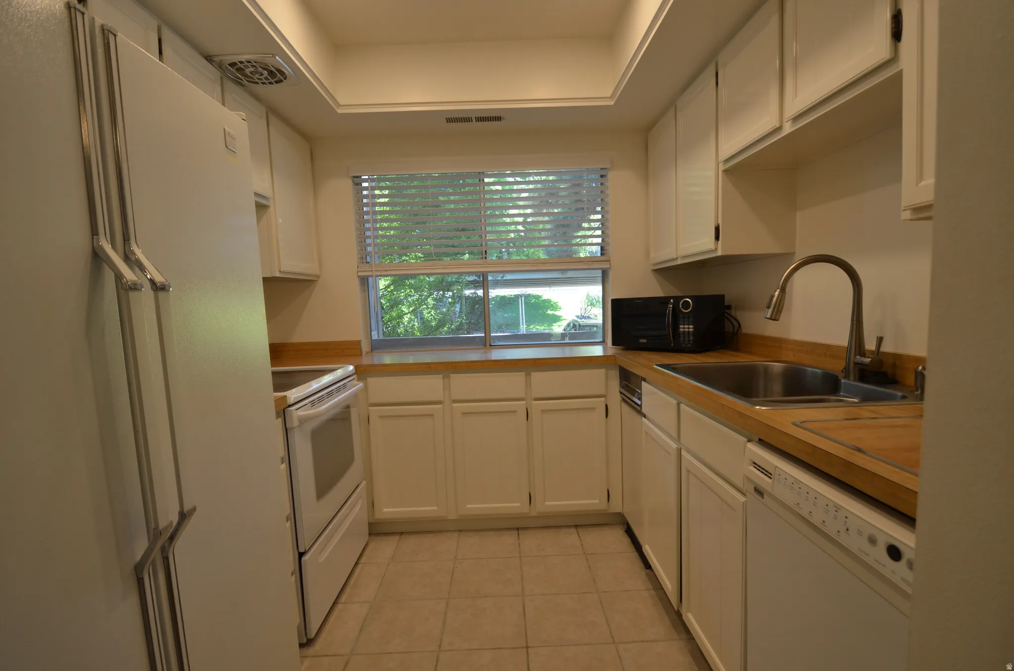 Galley kitchen featuring white cabinetry, light wood-finish countertops, and a tile floor