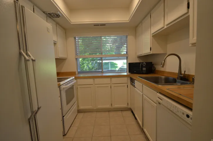 Galley kitchen featuring white cabinetry, light wood-finish countertops, and a tile floor