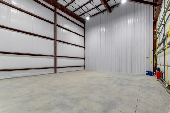Expansive open space featuring high ceilings, exposed metal beams, concrete flooring, and bright overhead lighting