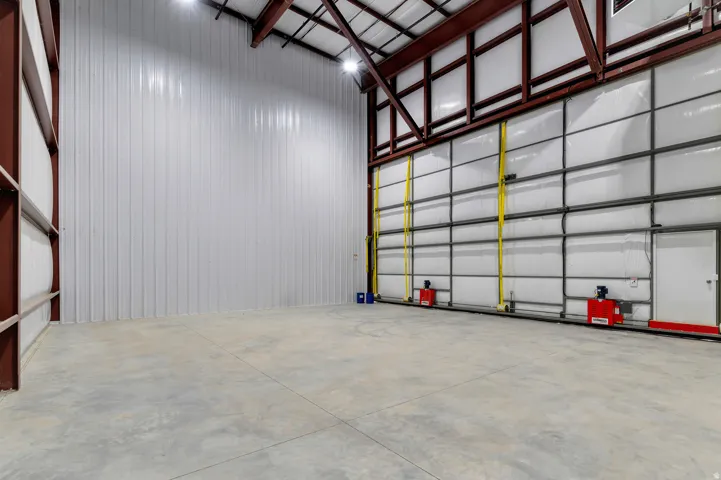 Spacious industrial interior featuring a concrete floor, high ceilings, exposed metal beams, and a large roll-up door