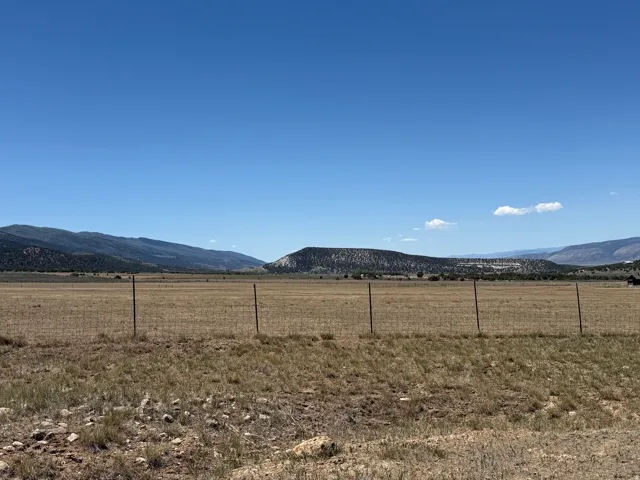 Expansive open land featuring a wire fence, brown and green vegetation, and distant mountains under a clear sky