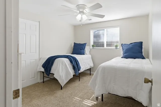 Carpeted room with a window featuring horizontal blinds, a white ceiling fan, and a white paneled door