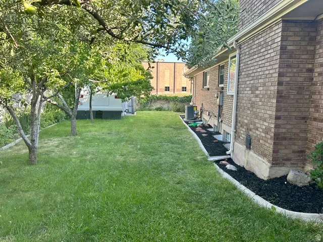Expansive backyard featuring a manicured lawn, established trees, and a brick exterior