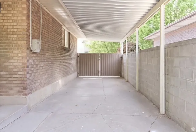 Covered carport featuring a concrete floor, brick wall, and privacy gate