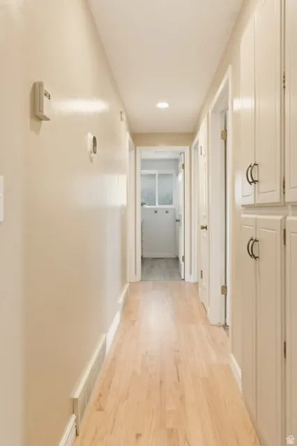 Hallway featuring wood-finish flooring, recessed lighting, and built-in cabinetry with dark hardware