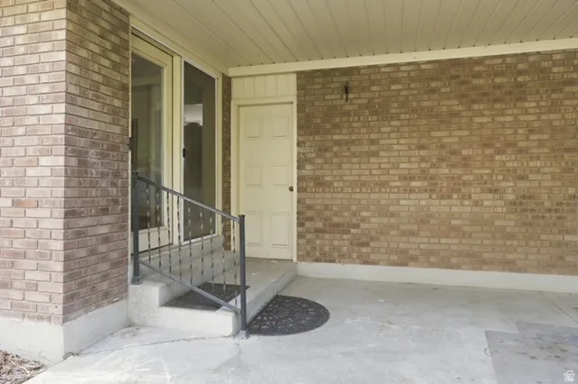 Brick facade entrance featuring a solid panel door, glass panel door, concrete steps, and a wrought iron handrail