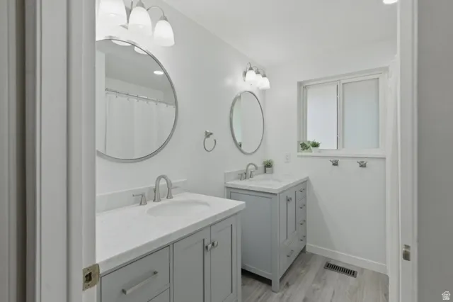 Bathroom with dual vanity sinks, light gray cabinetry, white countertops, and wood-finish flooring