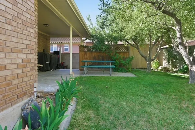 Backyard featuring a covered concrete patio, brick exterior, and a lush lawn with mature trees
