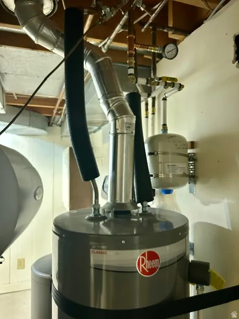 Water heater installation featuring a Rheem Classic tank, insulated piping, a wall-mounted expansion tank, and a pressure gauge