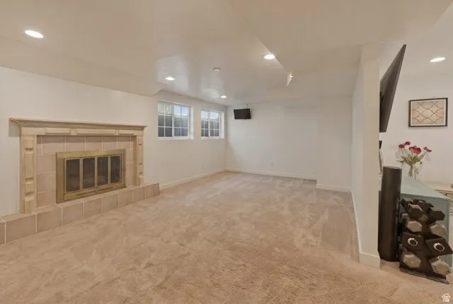 Spacious room featuring a tiled fireplace with a brass firebox, two windows, recessed lighting, and light-toned carpet