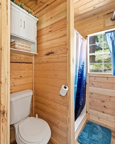 Wood-paneled bathroom featuring a white toilet, wall-mounted storage cabinet, and a shower stall with a window