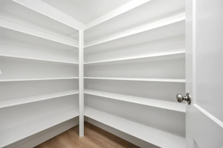 Walk-in pantry with extensive white shelving, wood-finish flooring, and a brushed nickel door handle