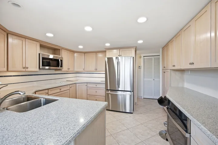 Open kitchen with light wood-finish cabinetry, speckled countertops, and stainless steel appliances