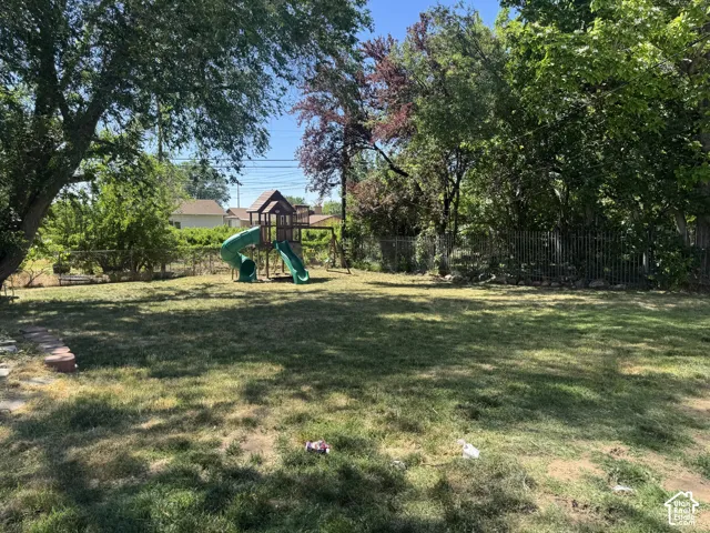 Expansive backyard featuring mature trees, a chain-link fence, and a swing set with two slides