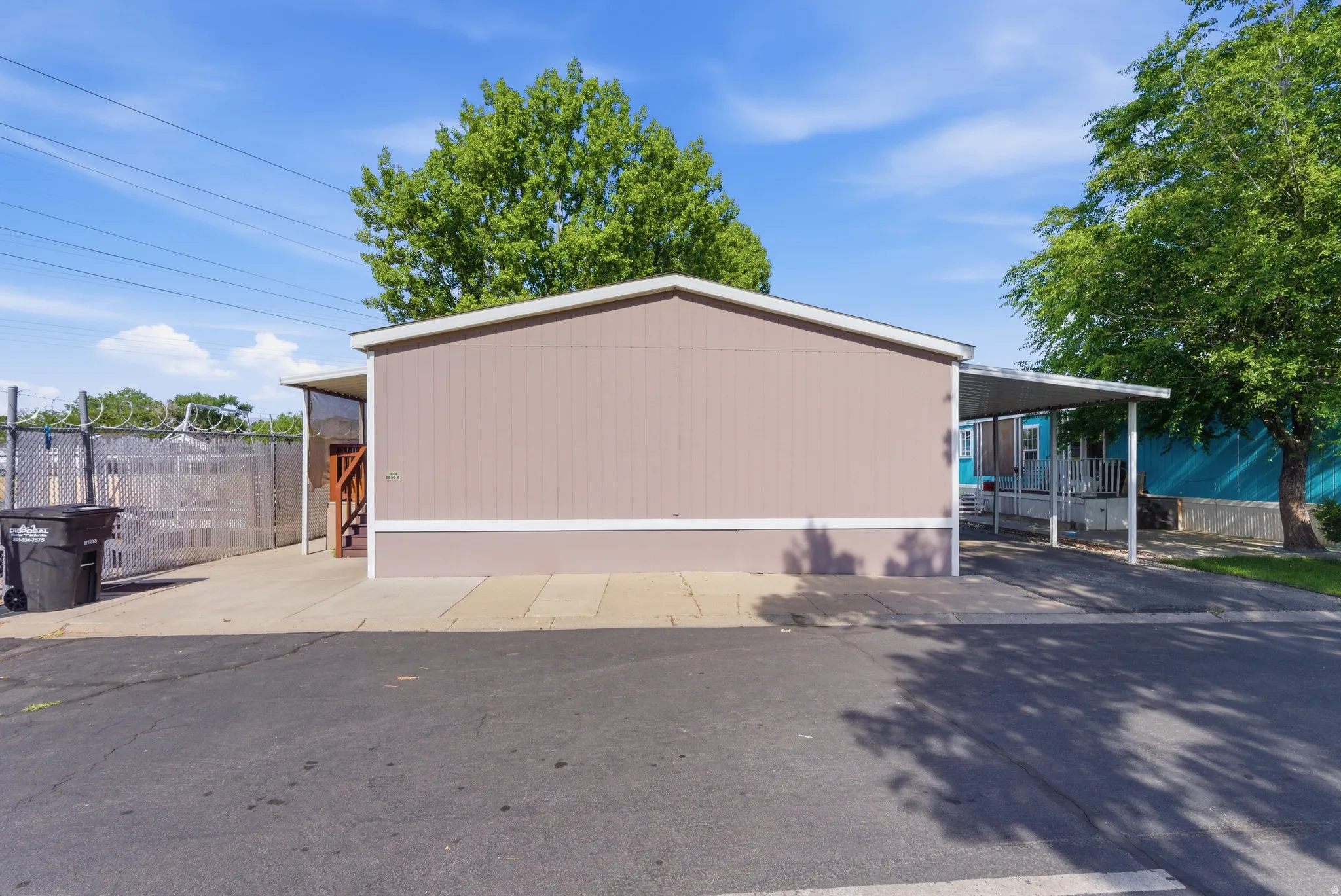 Exterior featuring tan siding, white trim, a covered carport, and a separate side entrance with wooden steps