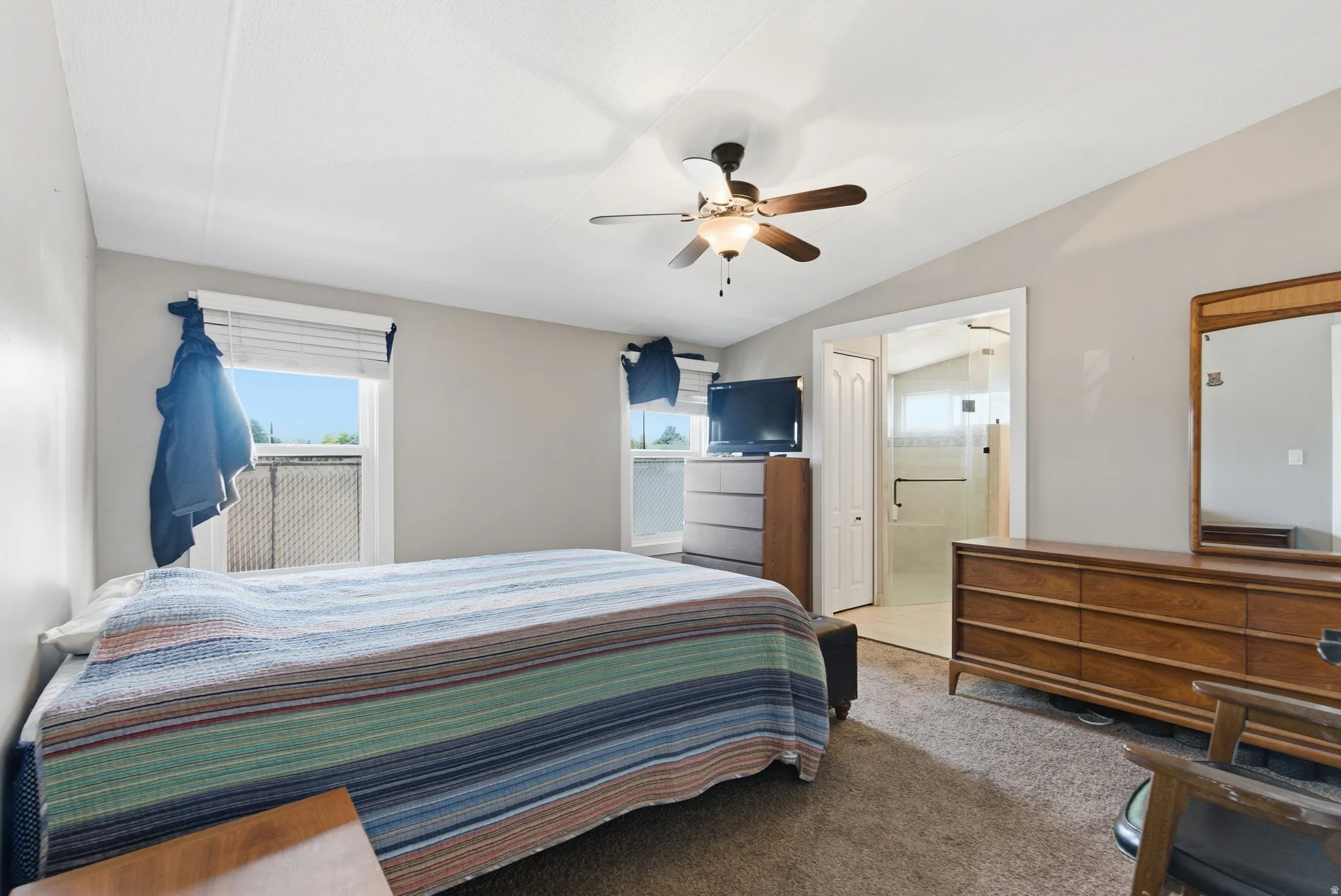 Carpeted bedroom featuring a ceiling fan, two windows with horizontal blinds, and direct access to a bathroom with a glass-enclosed shower