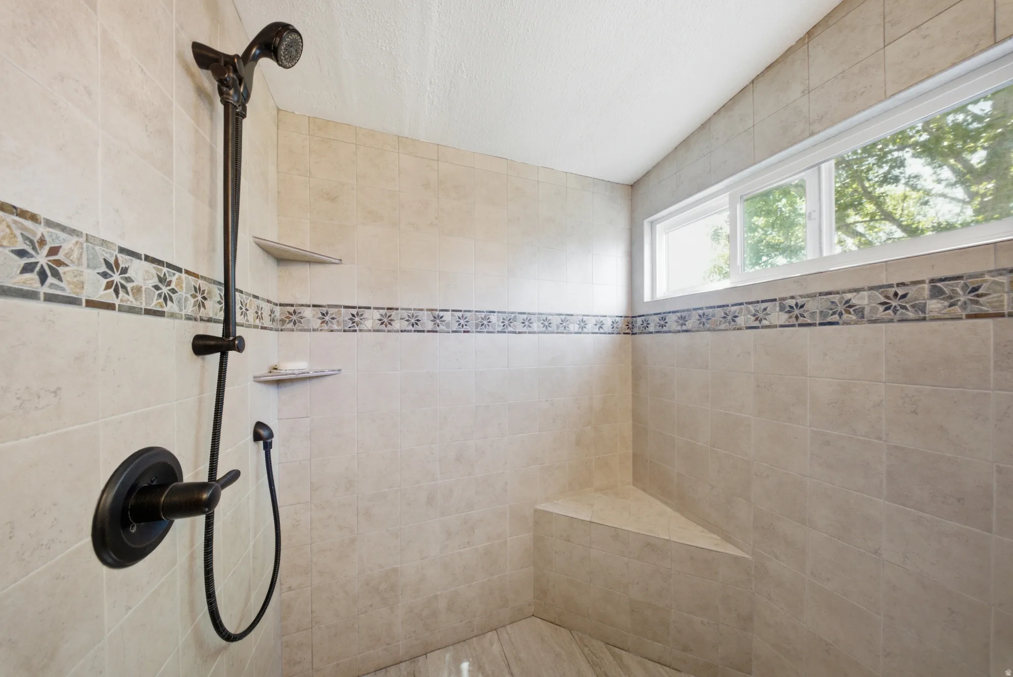 Tiled shower with a fixed showerhead, handheld shower, built-in bench, and two recessed shelves