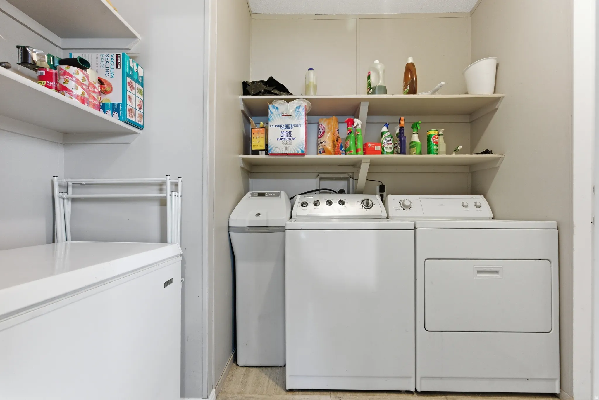 Utility area featuring integrated shelving, full-size washer and dryer, and a water softener system