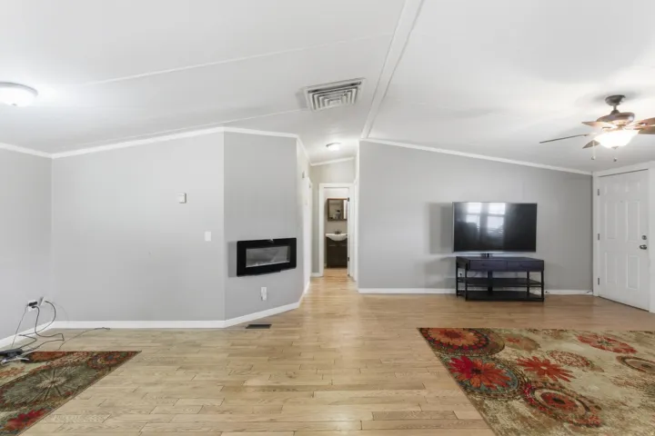 Open-concept living area featuring wood-finish flooring, a wall-mounted electric fireplace, and vaulted ceilings with crown molding