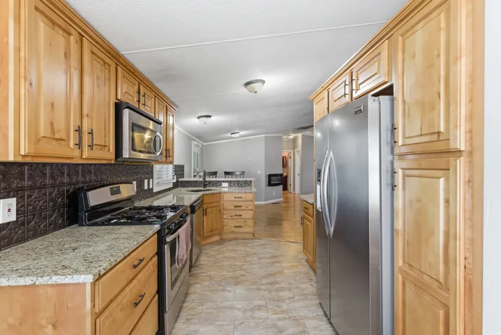 Kitchen featuring light wood cabinetry, granite-finish countertops, stainless steel appliances, a dark embossed backsplash, and tile flooring