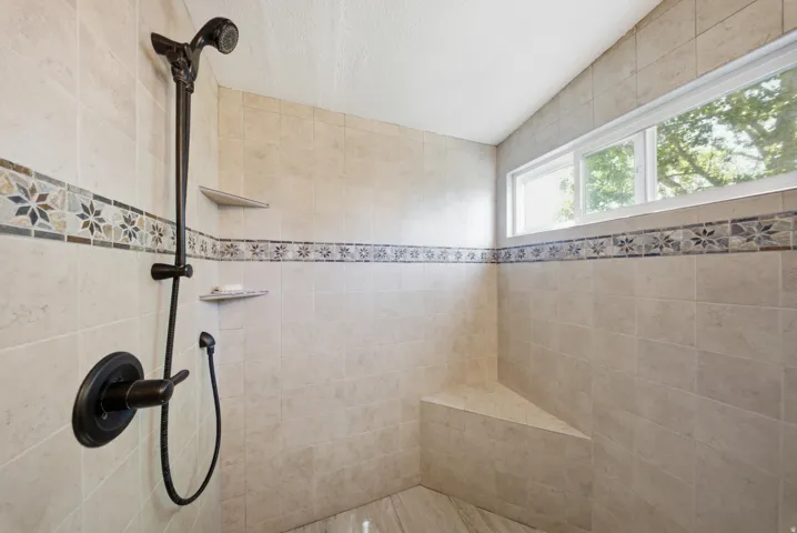 Tiled shower with a fixed showerhead, handheld shower, built-in bench, and two recessed shelves