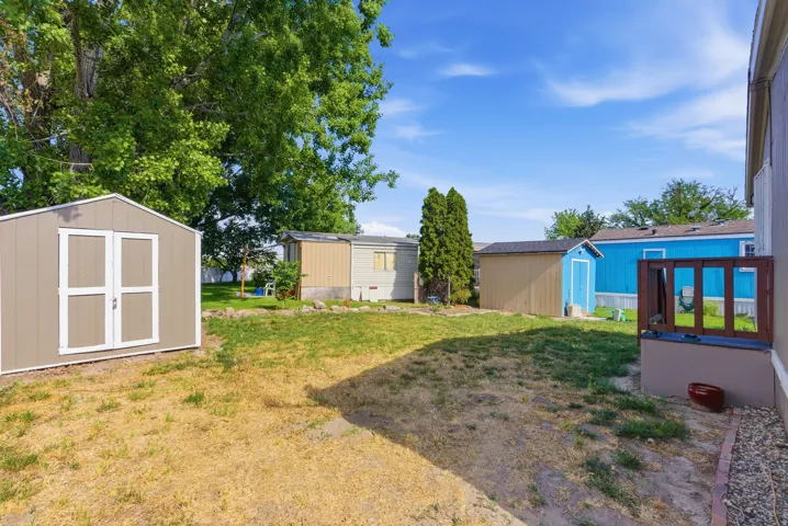 Spacious backyard featuring a tan storage shed with white trim, a privacy deck with wood railing, and mature trees